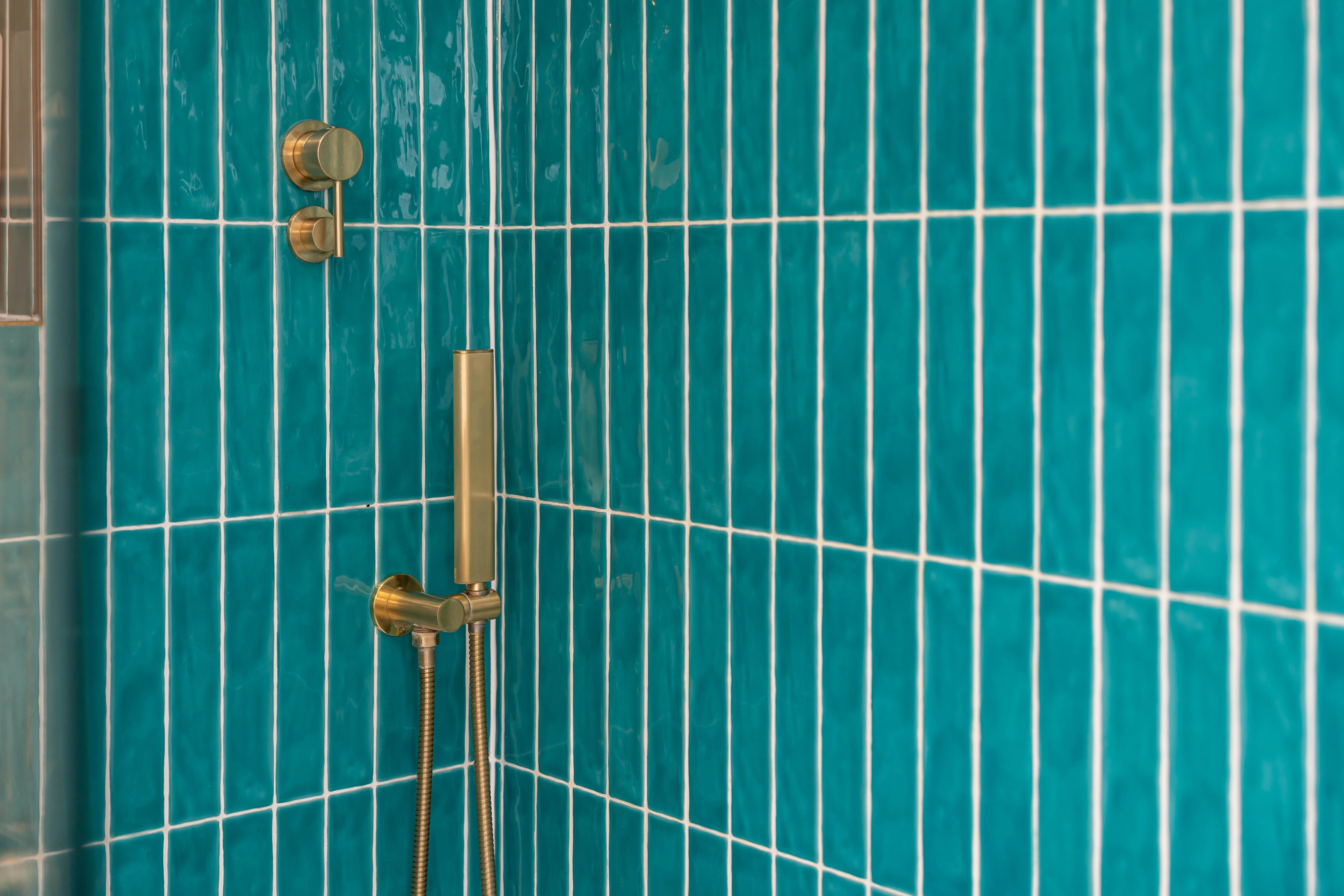 Close-up of a modern shower with turquoise tiles and gold fixtures, showcasing bathroom installation