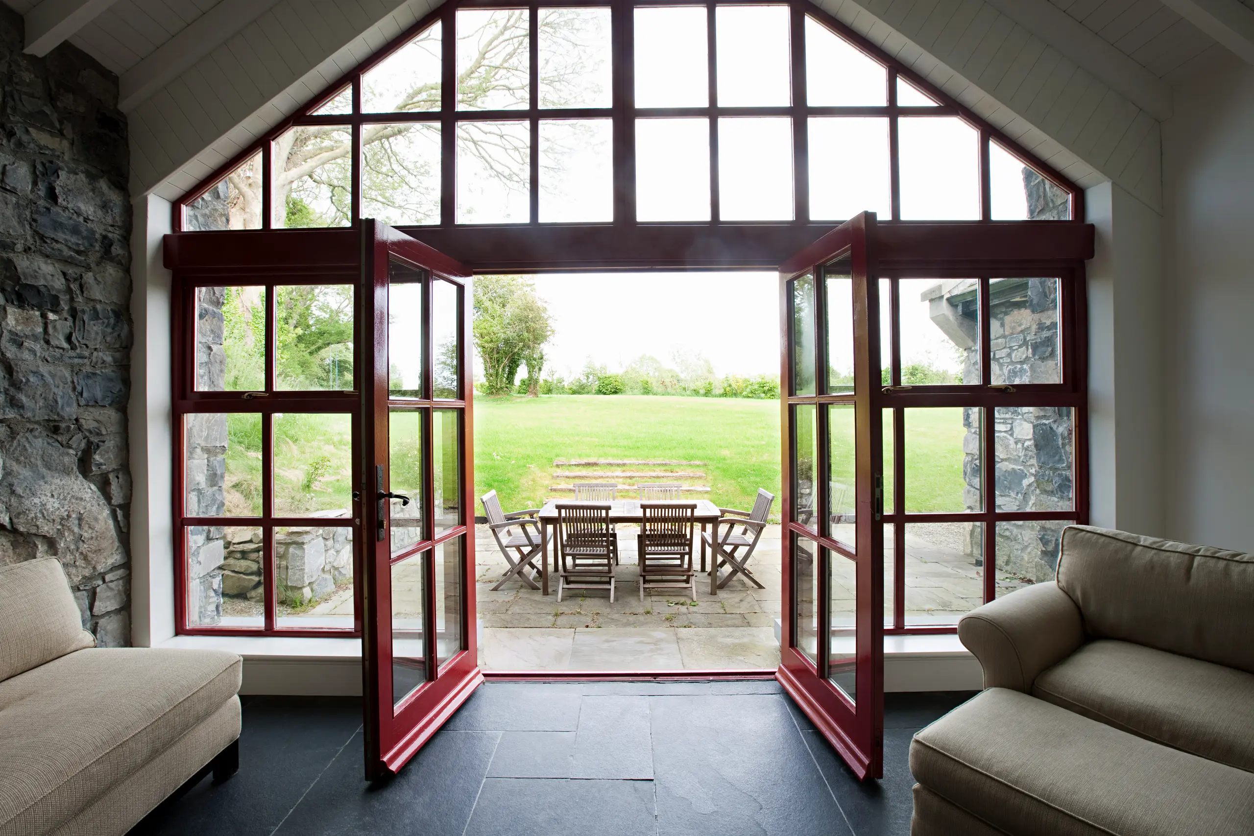 Open bi-fold doors leading to a backyard with a stone patio and wooden dining set