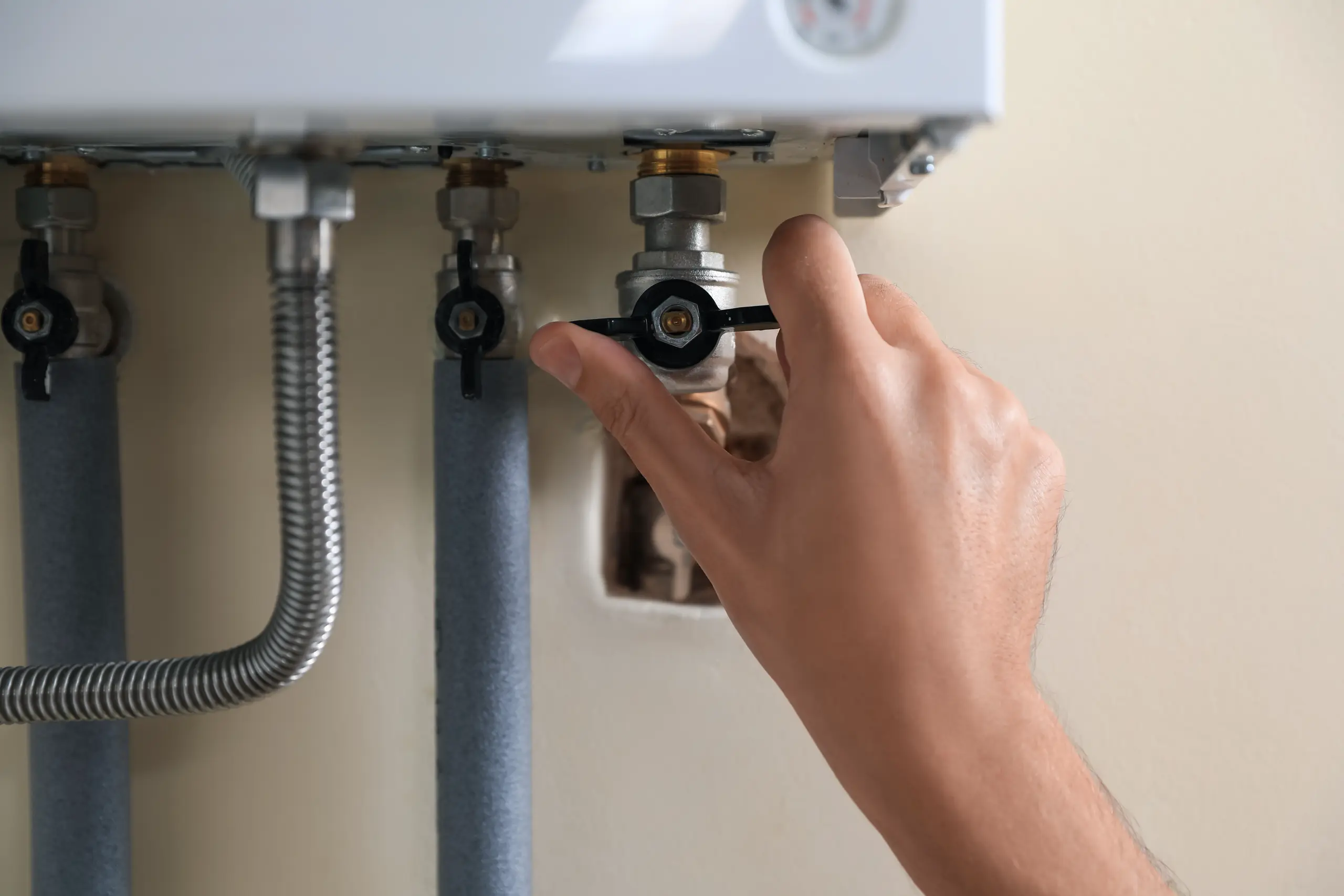 A hand adjusts a valve on a gas boiler, showcasing plumbing services in a home