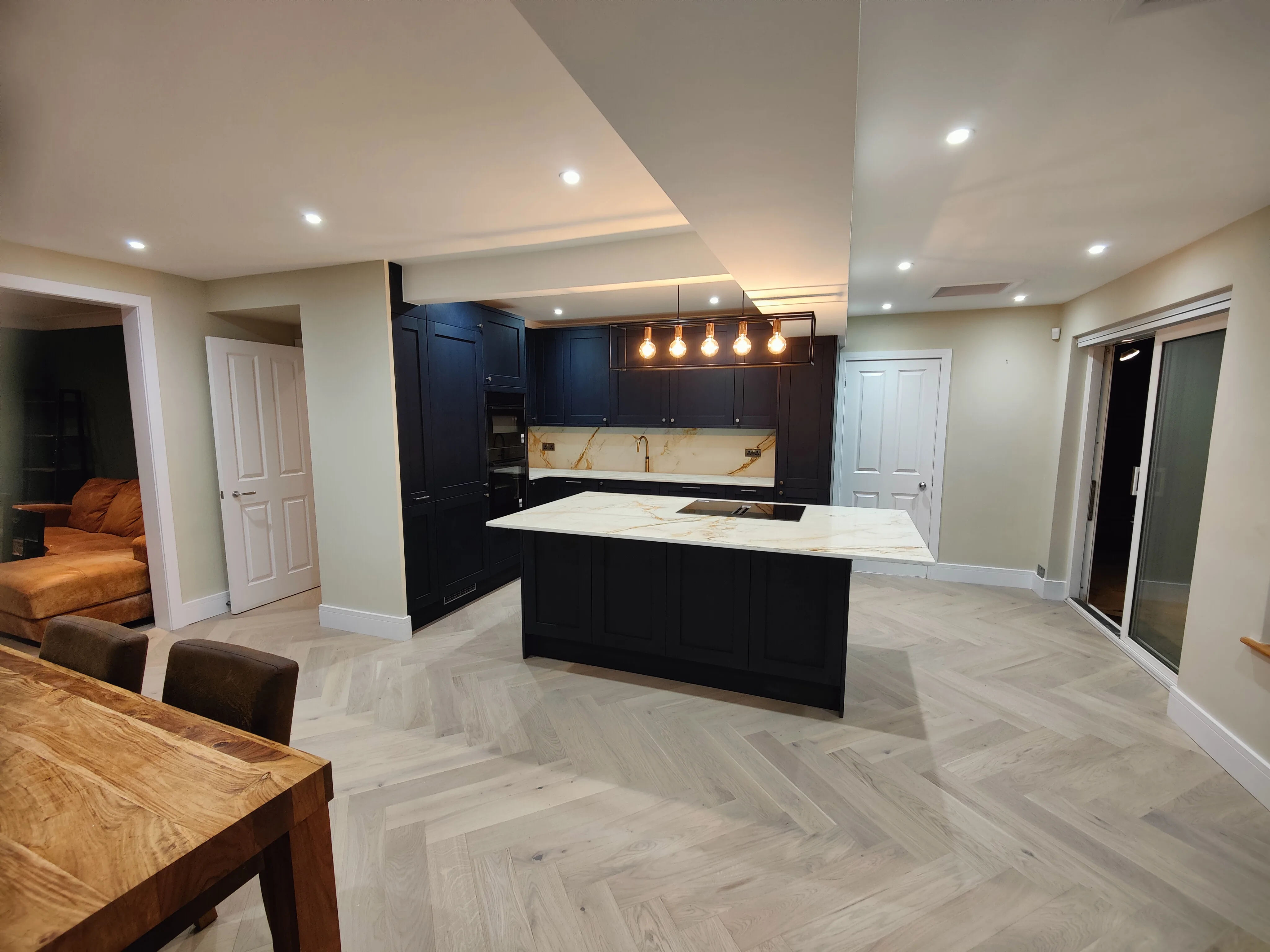 Modern kitchen refurbishment featuring dark cabinetry and herringbone wood flooring