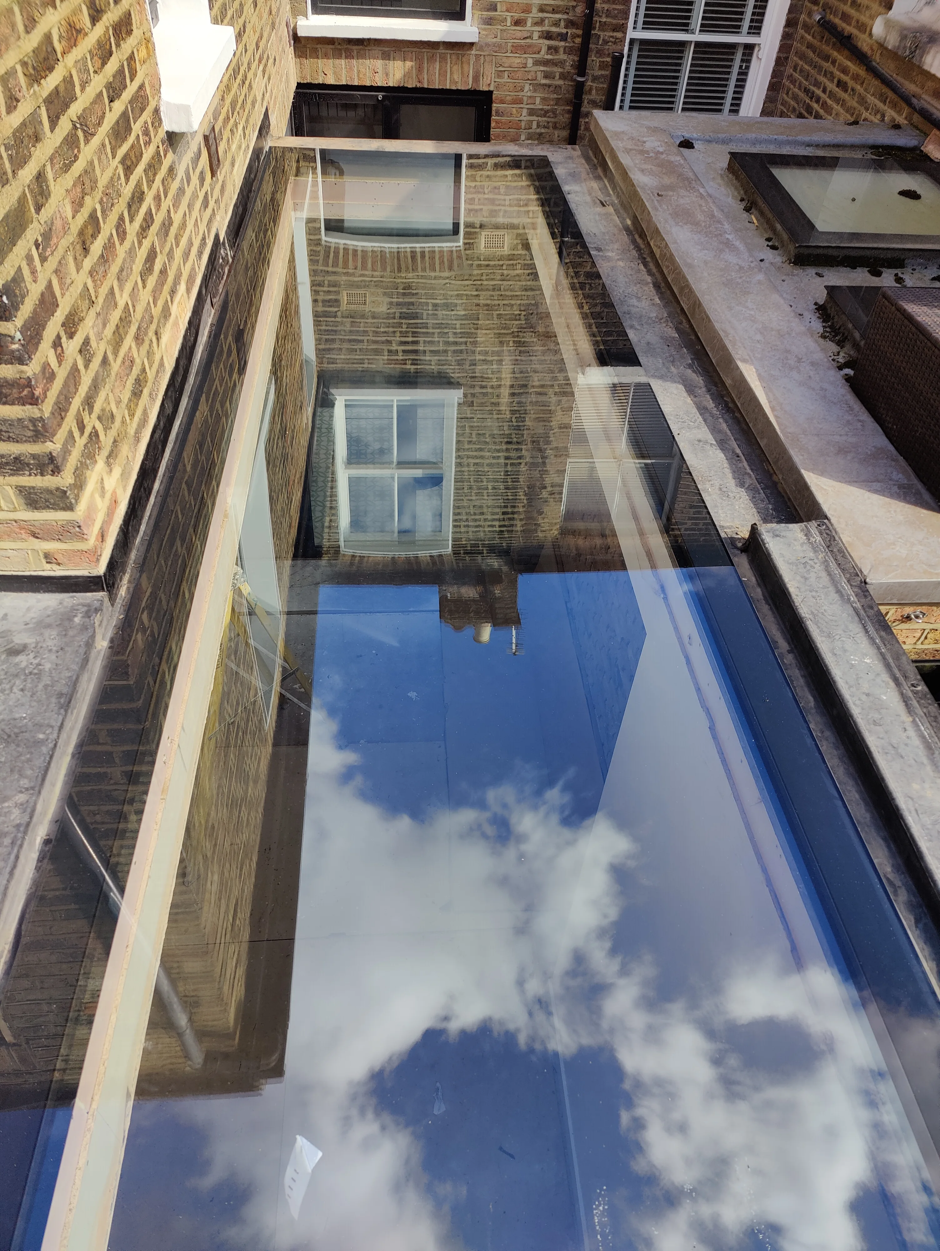 View of a glass roof installation reflecting the sky and surrounding buildings
