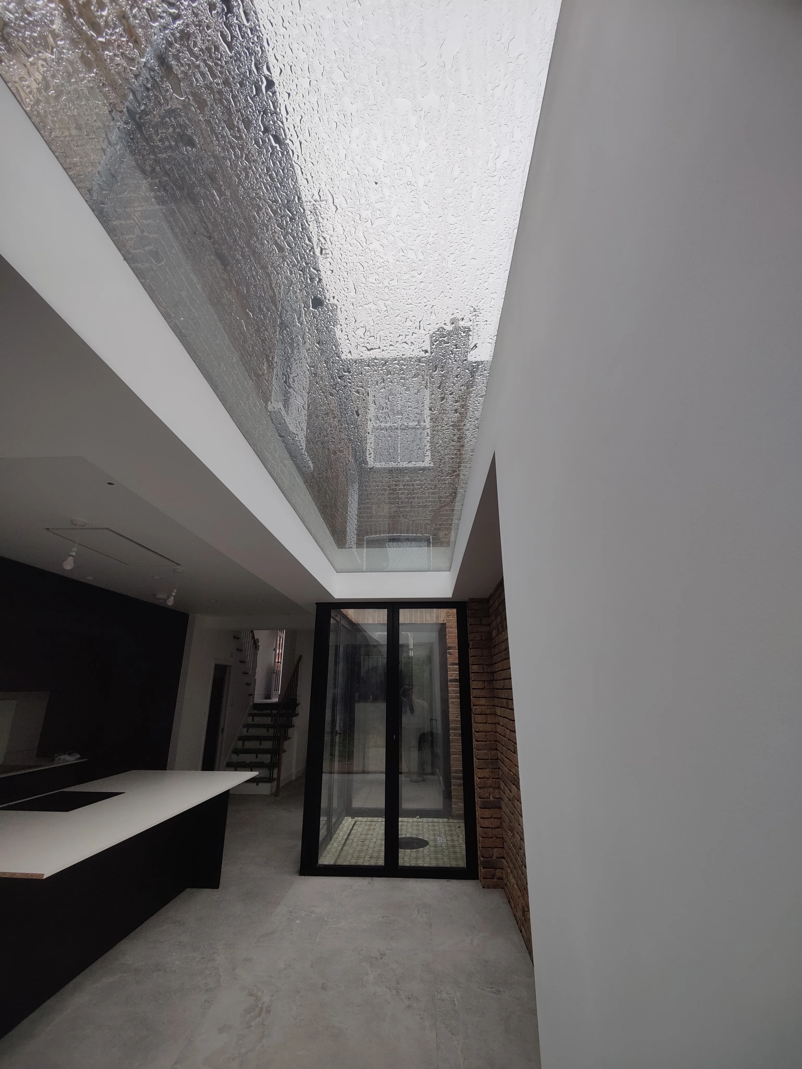 Interior view showing a modern kitchen with a glass roof and exposed brick wall